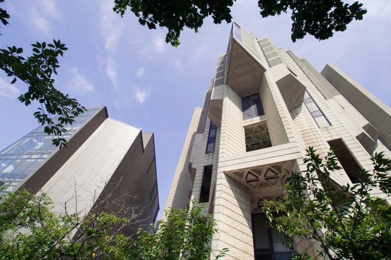 Robarts Library at the University of Toronto is shown surrounded by leafy foliage and backed by blue sky.