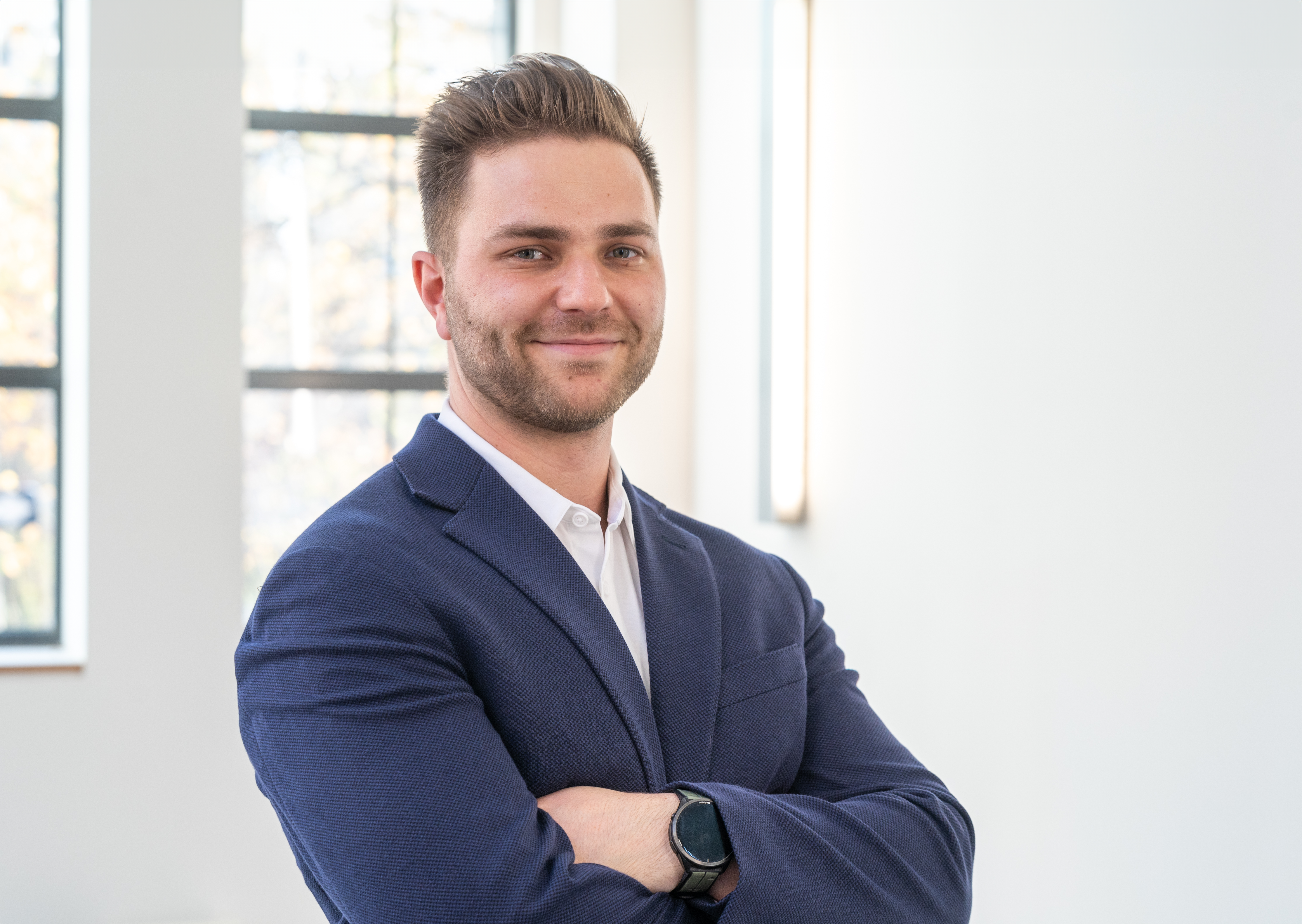 A headshot of Elliott crossing his arms and smiling. He is wearing a navy blazer and a white button-up shirt.